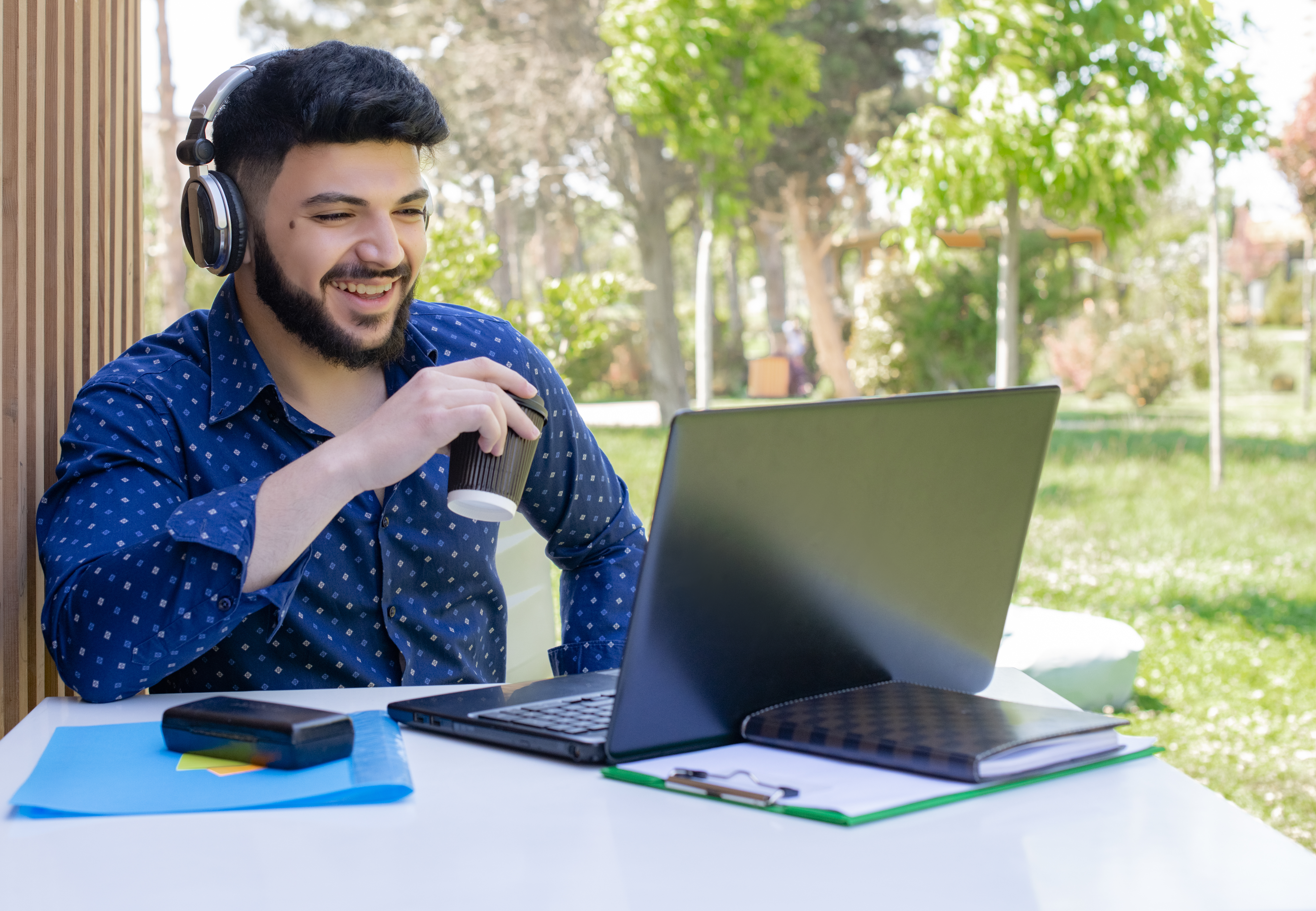 Man with headphones using a laptop at an outdoor venue while enjoying his coffee. Image on the online venue booking website's “About” page 